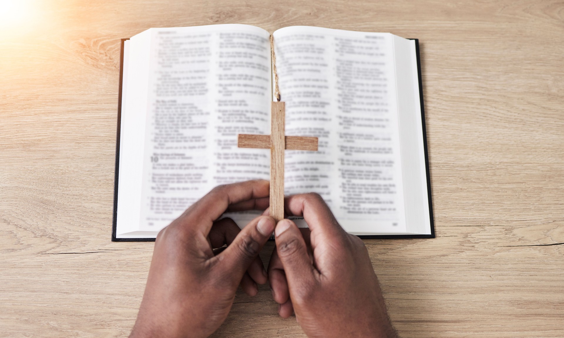 Bible, reading and cross with hands with book and religion study at home for worship and spiritual support. Faith, christian knowledge and person with gratitude, scripture education or above guidance